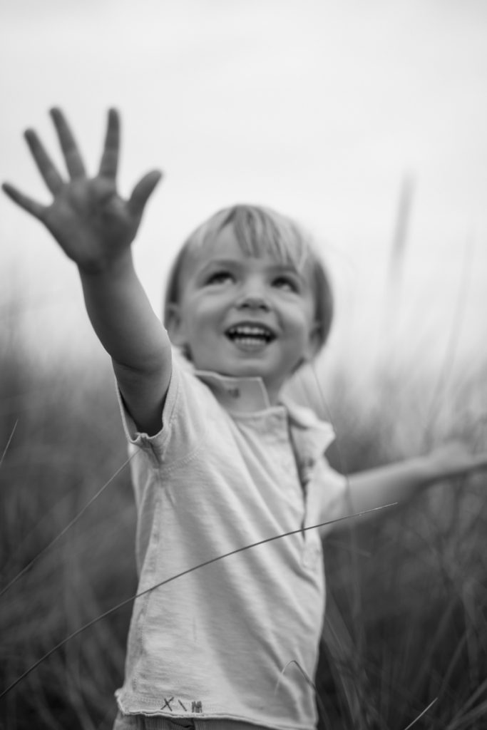 Black-and-white picture of a young boy with extended hands reaching towards the sky