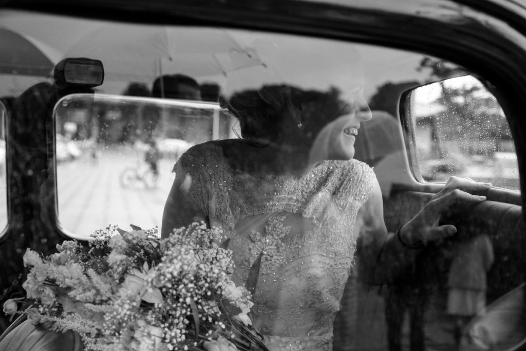 A bride in a car holding a bouquet of flowers and looking out the back window of the car