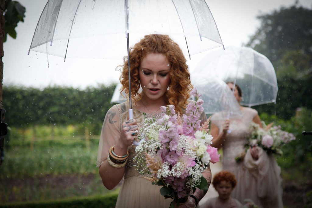 Picture of a curly red haired female holding a bouquet of flowers and a translucent umbrella above her head