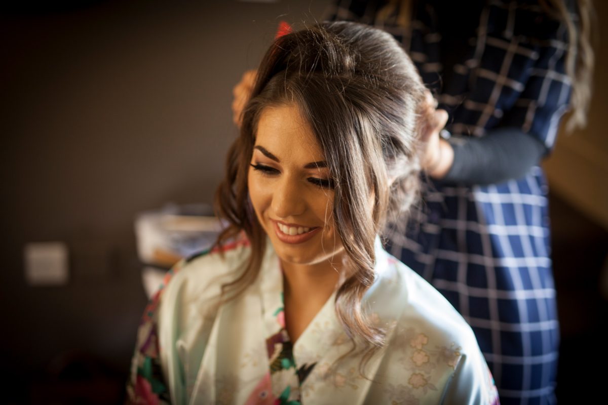 Bride in her dressing gown getting her hair done by makeup artist on morning of her wedding