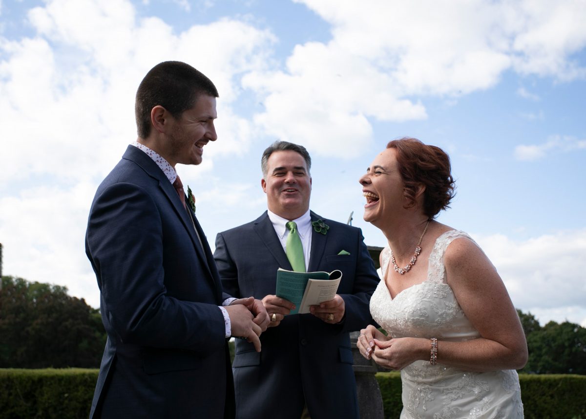 Bride laughing at the groom as he reads his vows